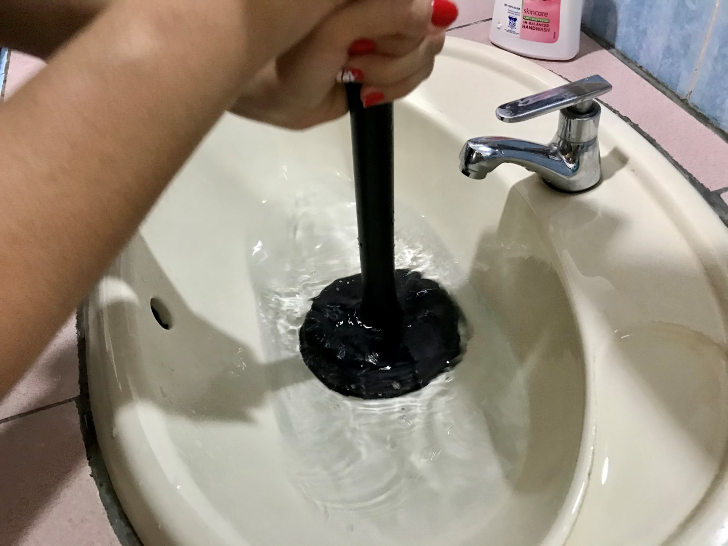 Homeowner using a plunger to clear a clogged bathroom sink.