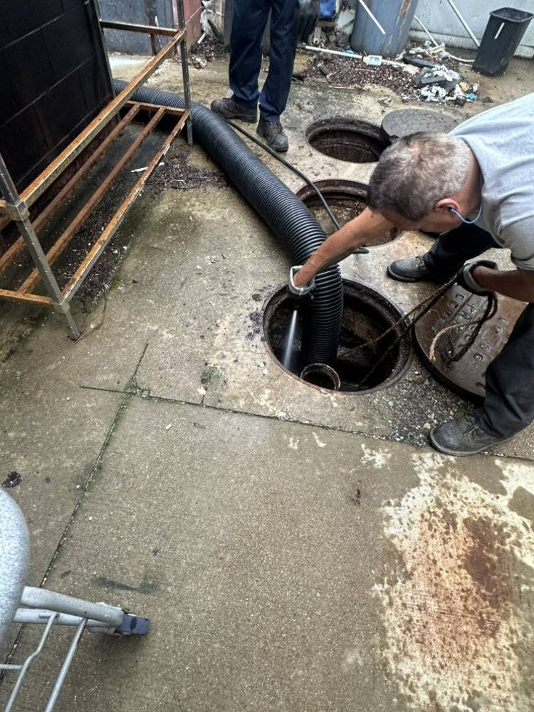 Technician performing hydro jetting on outdoor sewer line with safety gear.